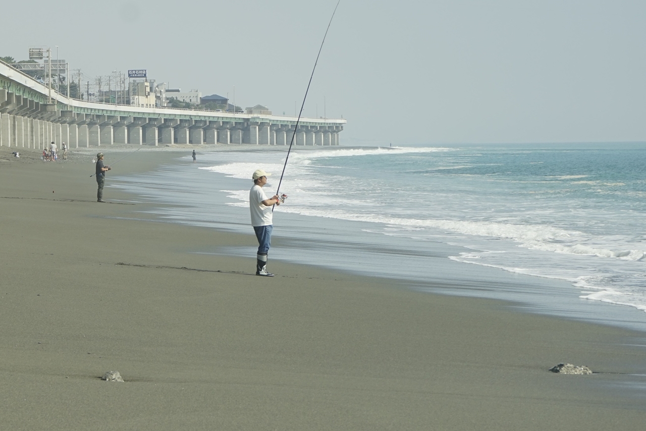 松浦果南が「そう、私は何となく分かる。」と発言したシーンの奥には釣りを楽しむ人がいっぱい！　劇中では小石が敷き詰められたような海岸線なのに対して、現実の「国府津海岸」は砂浜が広がっています